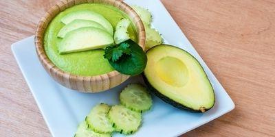 A green smoothie garnished with fresh avocado and cucumber slices