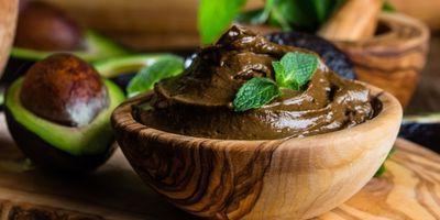 Wooden bowl filled with avocado chocolate mousse garnished with a mint leaf.